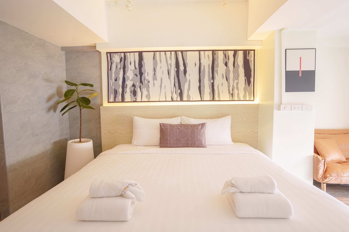 A modern hotel room with a large bed, a potted plant, and a minimalist artwork above the bed.