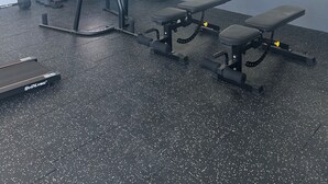 Ein Fitnessraum mit Trainingsgeräten, einer Bank und einem Spiegel, der den Raum wiedergibt.
