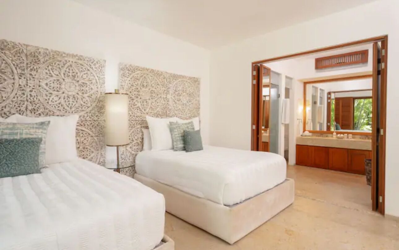 A hotel room with two beds, a large mirror, and a view of the bathroom.