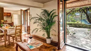 A dining area with wooden furniture, a potted plant, and a glass door leading to an outdoor patio with a hammock and a table. - Villa Sorrentina With Panoramic Terrace (Massa Lubrense)