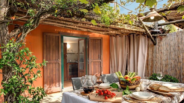 An outdoor dining area with a table set for two, surrounded by greenery and a rustic building. - Villa Sorrentina With Panoramic Terrace (Massa Lubrense)