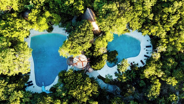 An aerial view of a resort with two large swimming pools surrounded by lush greenery, a central gazebo, and a small building. - VILLA ESCONDIDA - RIVIERA MAYA - LUXURY HOME WITH HIGH QUALITY DESIGN (Cancún)