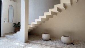 A modern interior with a staircase, a potted plant, and two large vases on a pebble surface. - VILLA ESCONDIDA - RIVIERA MAYA - LUXURY HOME WITH HIGH QUALITY DESIGN (Cancún)