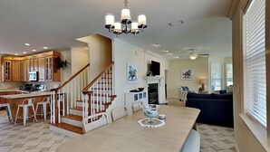 A spacious kitchen with a central island, wooden staircase, and a dining area with a chandelier. - Corner Castle by Southern Vacation Rentals (Destin)
