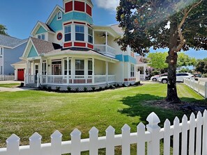 A two-story house with a wrap-around porch, a red garage, and a white picket fence. - Corner Castle by Southern Vacation Rentals (Destin)