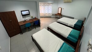 Une chambre d’hôtel avec trois lits, un bureau, une chaise, une télévision et une fenêtre avec des rideaux.