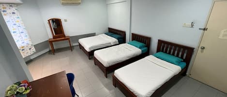 A hotel room with three single beds, a wooden table with a vase of flowers, a chair, and a window with curtains.