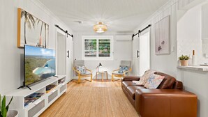 A living room with a TV, two chairs, a sofa, a ceiling fan, and a window with blinds.