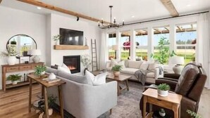 A spacious living room with a fireplace, large windows, and a modern fireplace mantel. - Luxe Barndominium - Mtn Views! "Hemlock" (Columbia Falls)