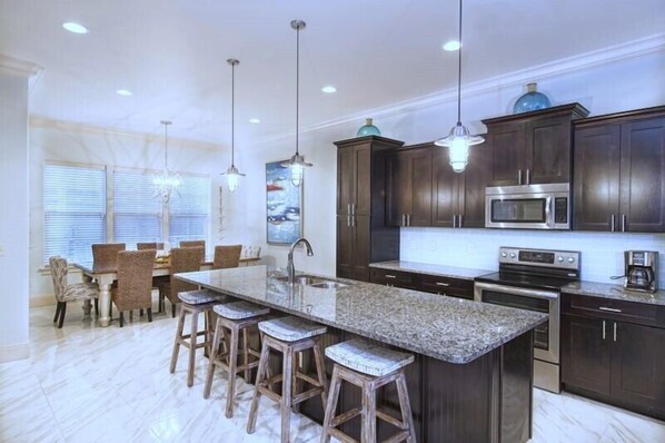 A modern kitchen with dark wood cabinets, a granite countertop, stainless steel appliances, and pendant lighting. - 20% Discount, 4BR Pool, $700 in freebies incl golf (Miramar Beach)