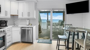 Une cuisine moderne avec des meubles blancs, une machine à café et un lave-vaisselle. On y trouve également un coin repas avec une table et des chaises, ainsi qu’un téléviseur fixé au mur.