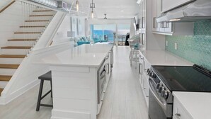 Une cuisine moderne avec des meubles blancs, un îlot central et une vue sur l’extérieur.