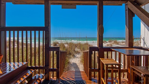 Een houten terras met banken en tafels, met uitzicht op een strand.