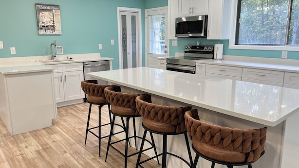 A modern kitchen with a large island, white cabinetry, and a teal accent wall. - 5 BR King Beds Game Room Yard Family Home Explore DC Quantico Stafford  (Stafford)