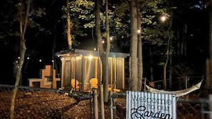 A wooden cabin with a sign reading "Welcome to our Garden" in a forested area at night. - 5 BR King Beds Game Room Yard Family Home Explore DC Quantico Stafford  (Stafford)