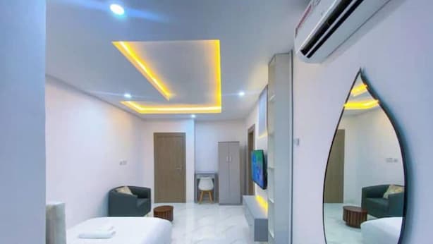 A modern hotel room with a large bed, a seating area with a sofa and armchairs, a small table, and a mirror. - Studio(S7) @ LEKKI PHASE 1. 24/7 AC. By NgoZiLiving


 (Lekki, phase 1)