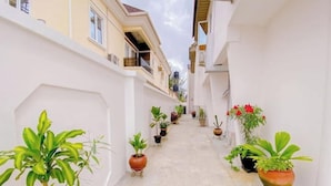 A narrow, white-walled alley with potted plants on either side, leading to a building with balconies. - Studio(S7) @ LEKKI PHASE 1. 24/7 AC. By NgoZiLiving


 (Lekki, phase 1)