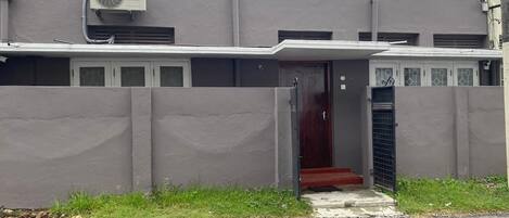 A building with a grey facade, a red door, and a small entrance with steps.
