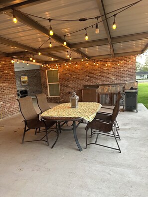 Une terrasse extérieure avec un mur en briques, un espace salon abrité et un barbecue.