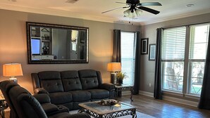 A living room with a black leather sofa, a glass coffee table, and a ceiling fan. - Cajun Country Escape  (Gonzales)