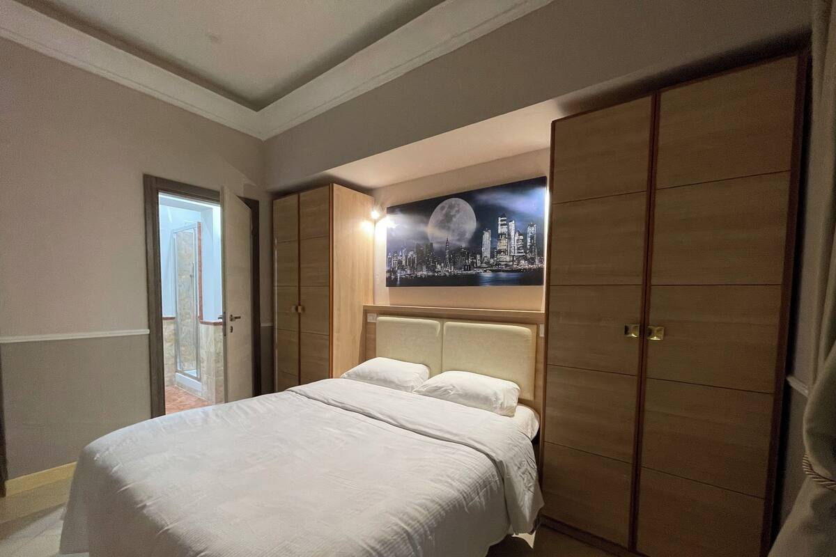 A hotel room with a large bed, a cityscape painting on the wall, and a wardrobe.