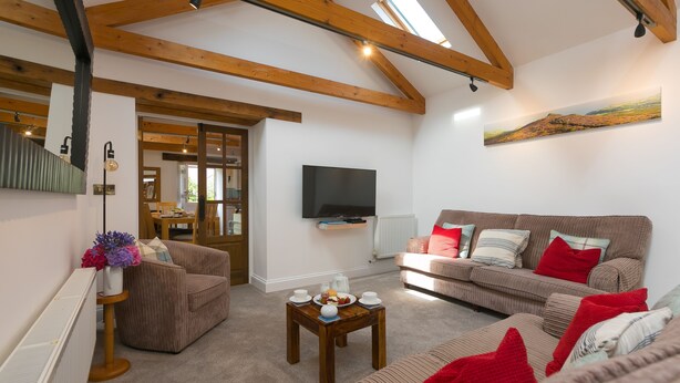 Ein Wohnzimmer mit einem braunen Sofa, einem Holztisch und einem flachbildfernseher an der Wand.