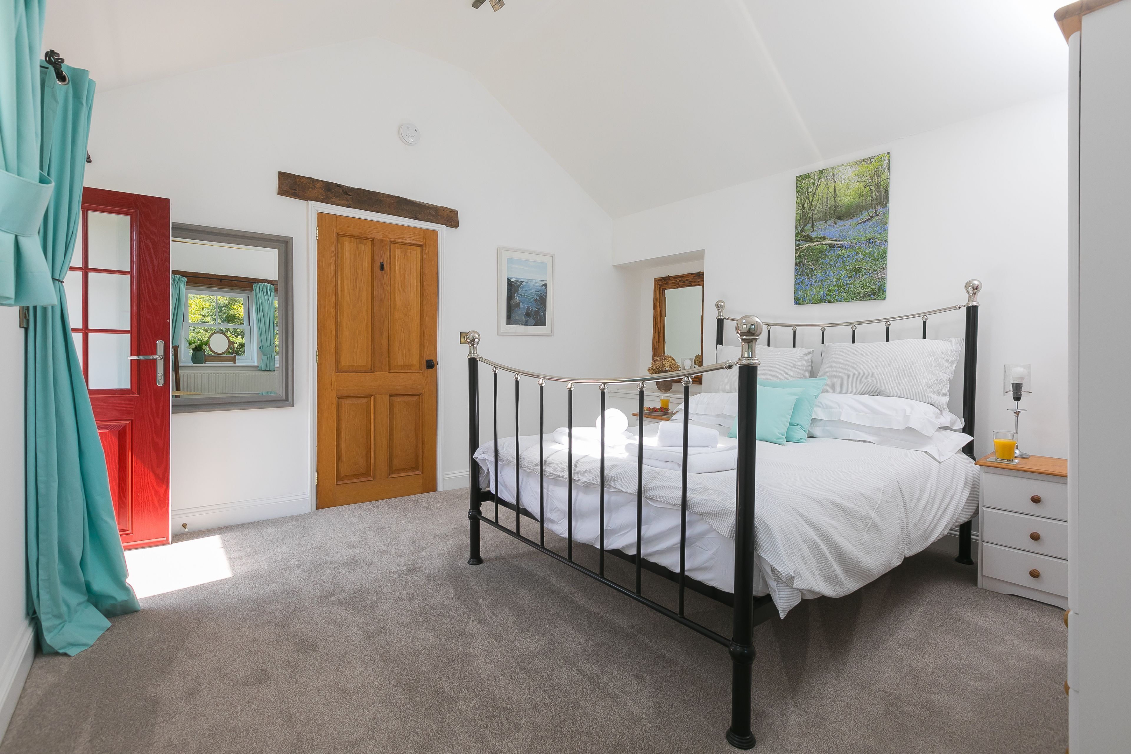 Une chambre à coucher avec un lit, une table de chevet, une porte en bois et une fenêtre avec des rideaux.