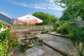 Eine Gartenpatio mit einem Holztisch und einem pinken Sonnenschirm mit dem Aufdruck 'FEVER TREE'.