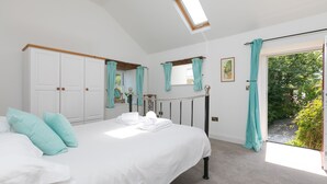 Ein Schlafzimmer mit einem großen Bett, weißen Vorhängen, einem Oberlicht und Blick ins Grüne.