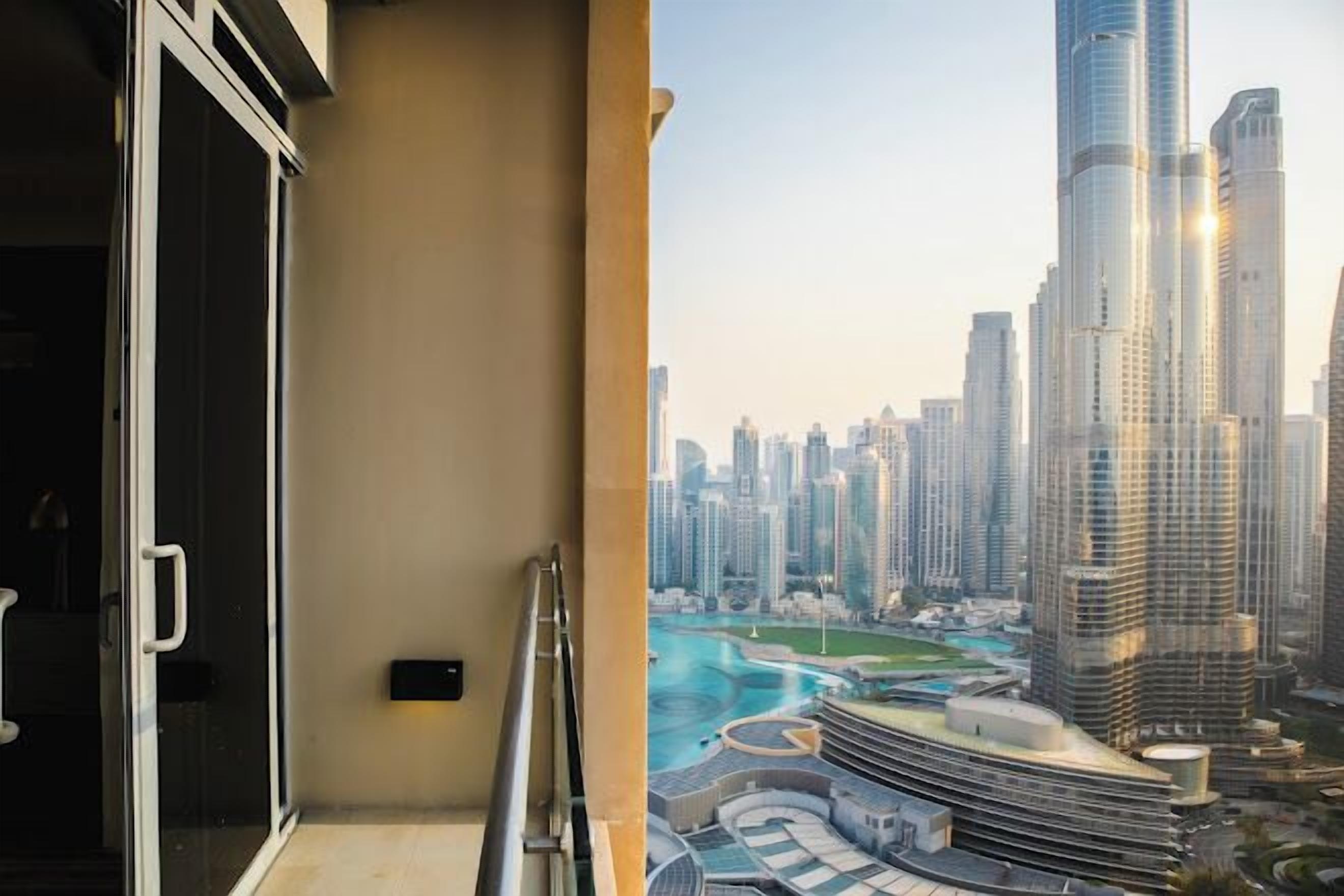 A balcony with a glass door, a metal railing, and a view of a modern cityscape with high-rise buildings.