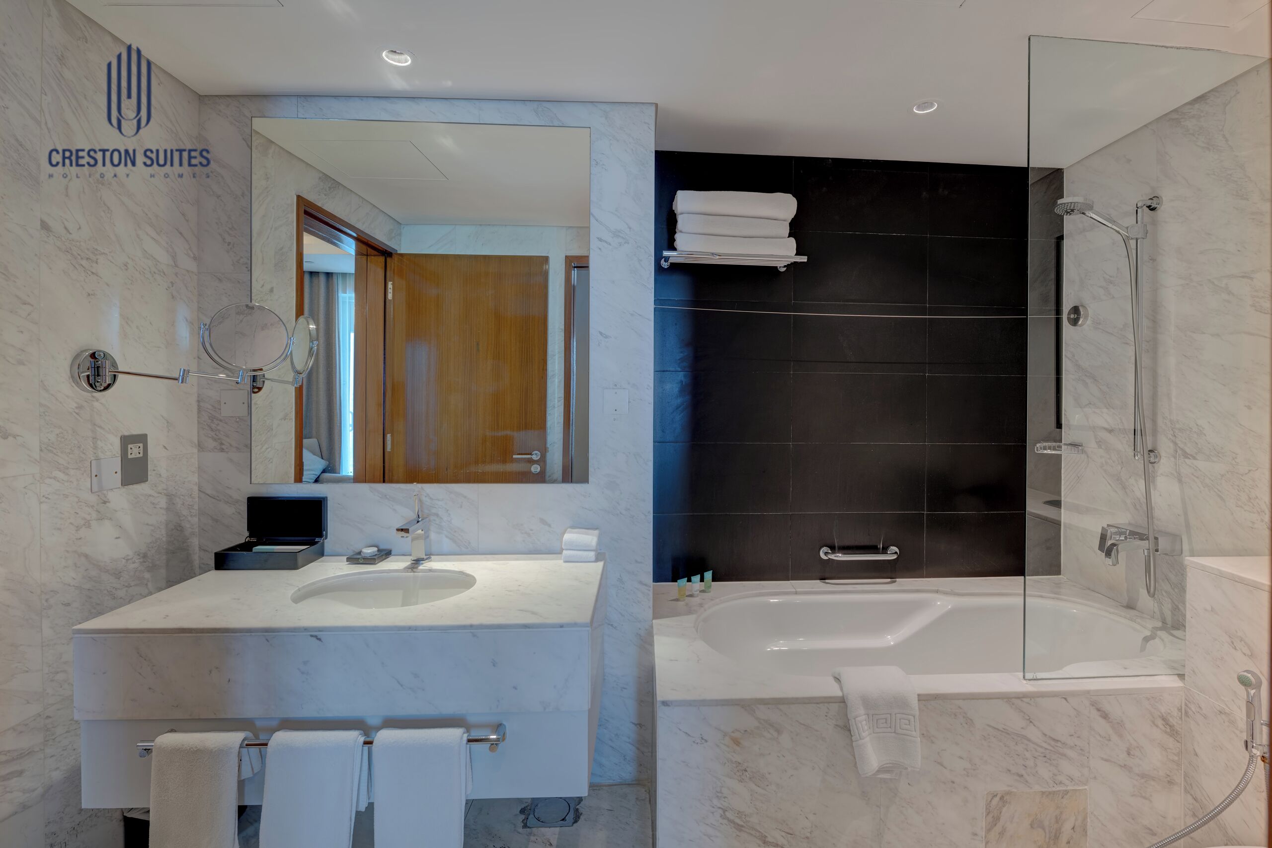 A modern bathroom with a marble vanity, a large mirror, a glass-enclosed shower, and a dark accent wall.