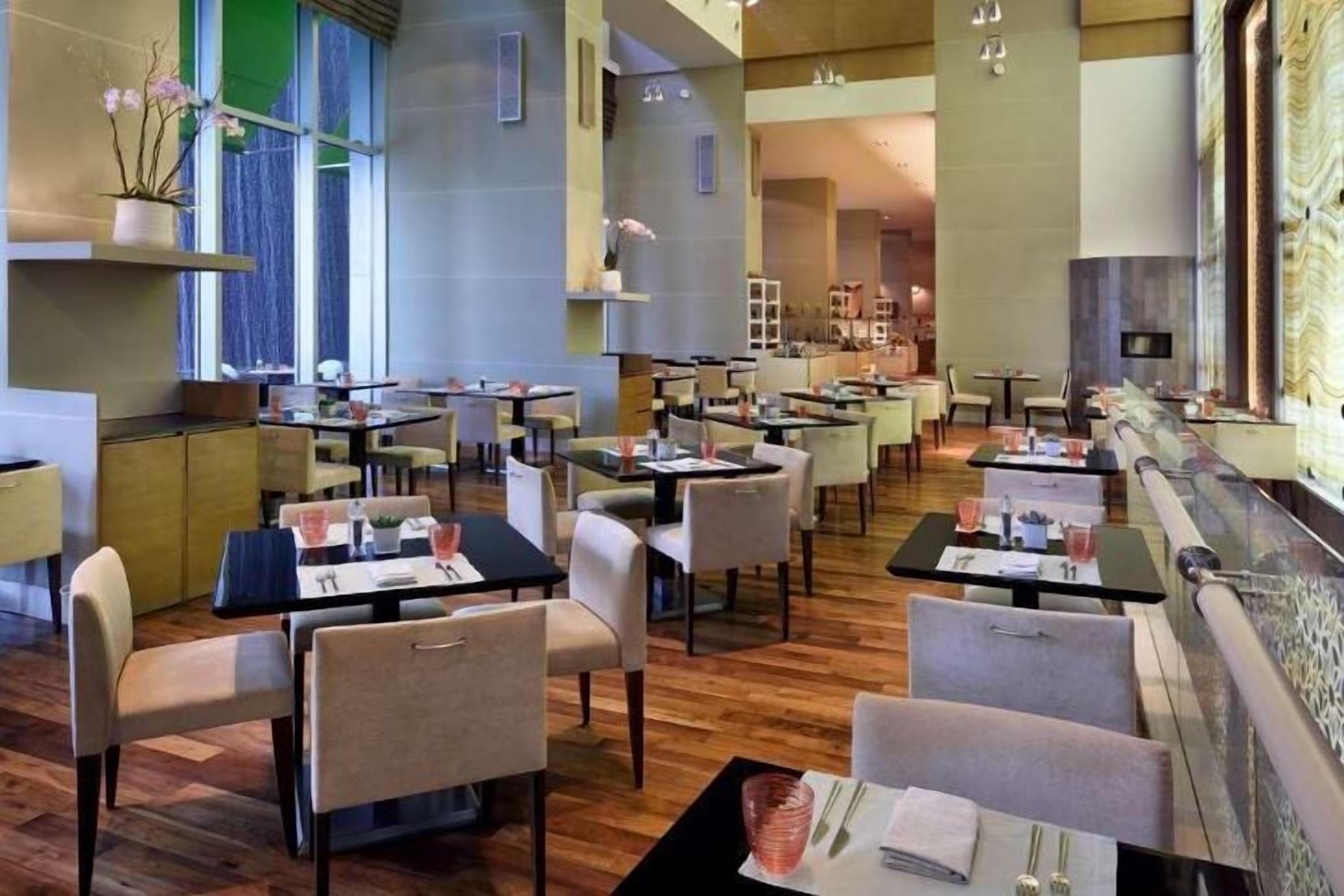 A modern restaurant with multiple tables and chairs, a wooden floor, and a large window with a view.