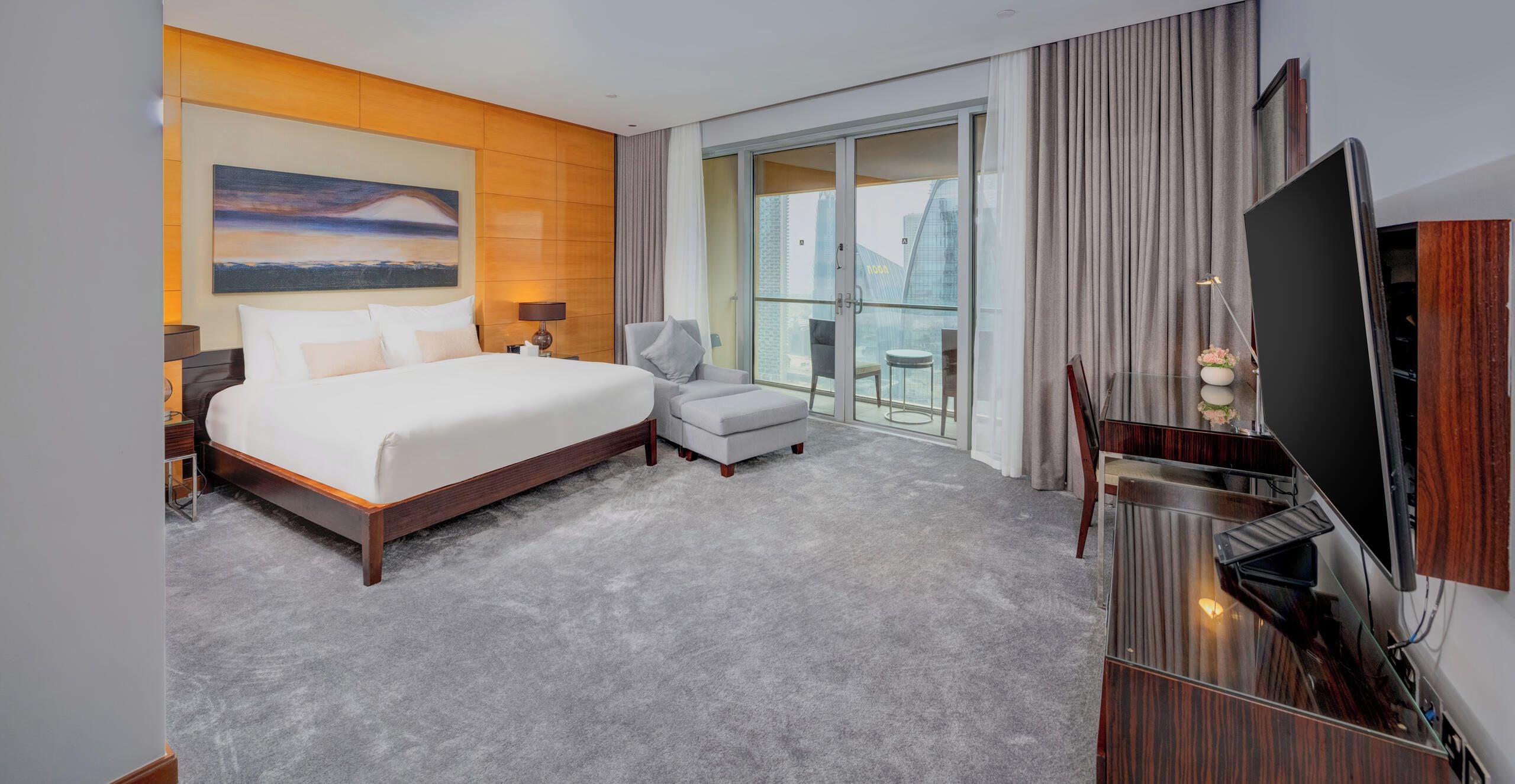 Une chambre d’hôtel avec un grand lit, une chaise, un bureau, une télévision et une vue sur la ville, visible à travers une porte vitrée.
