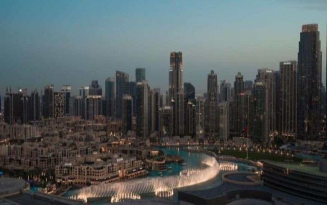 A cityscape with high-rise buildings and a waterfront area with a fountain.