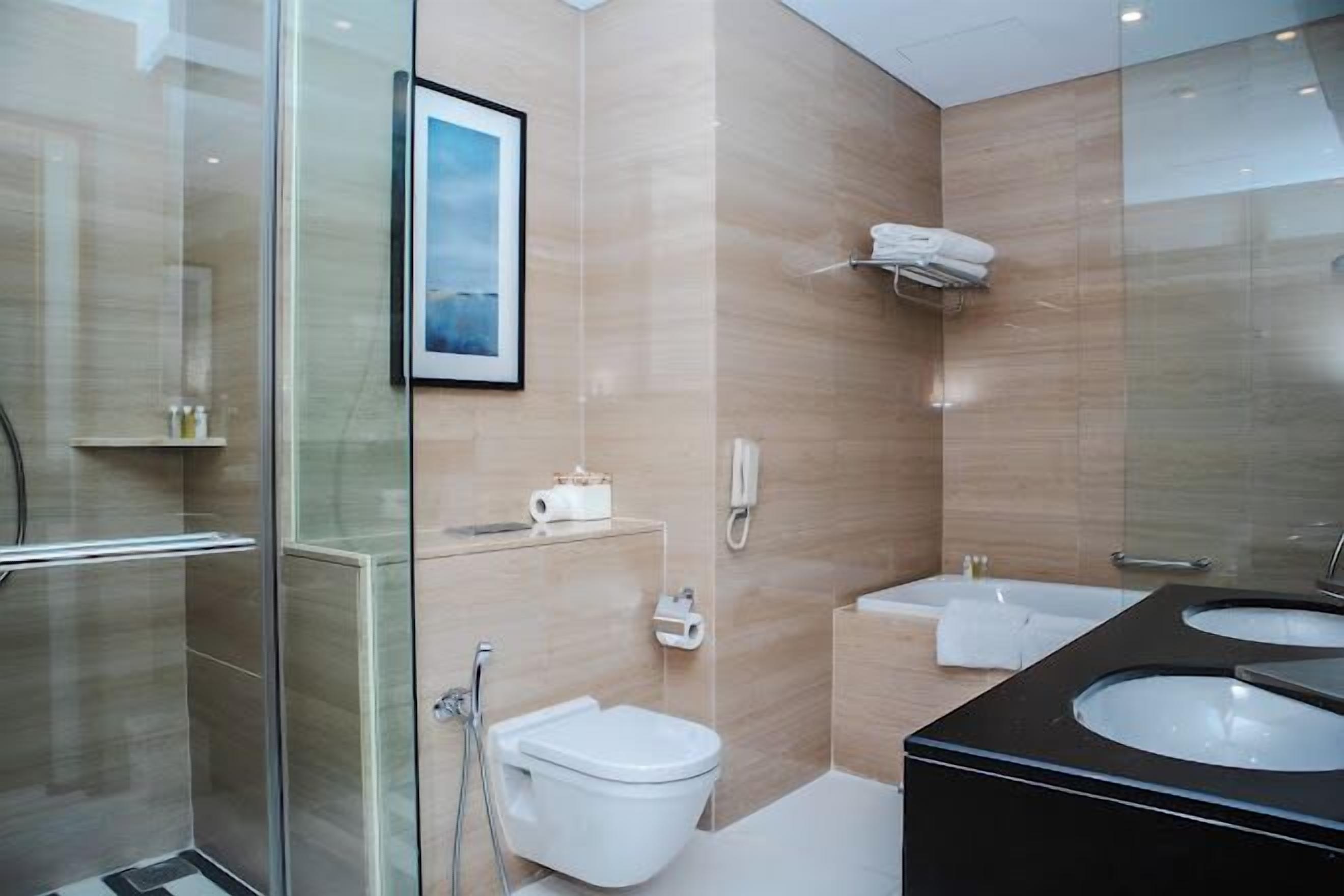 A modern bathroom with a glass shower enclosure, a toilet, a bidet, and a vanity with two sinks.