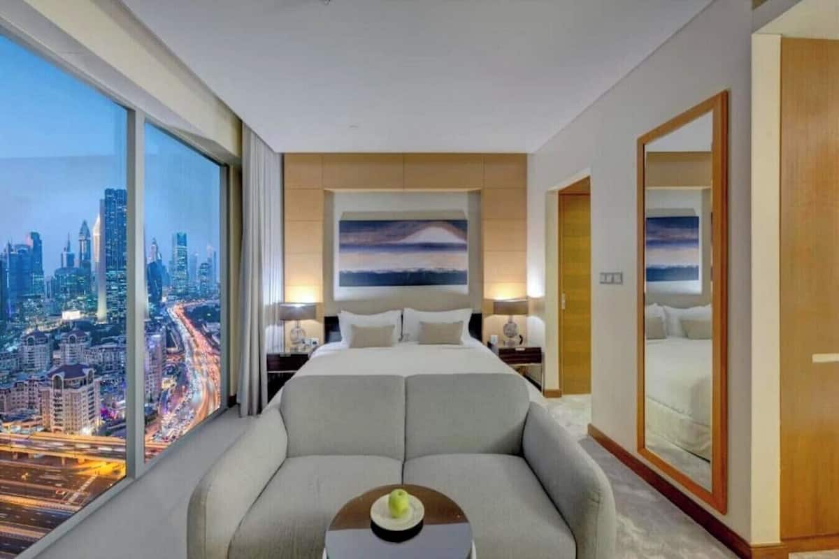 A modern hotel room with a large bed, a sofa, and a city view.