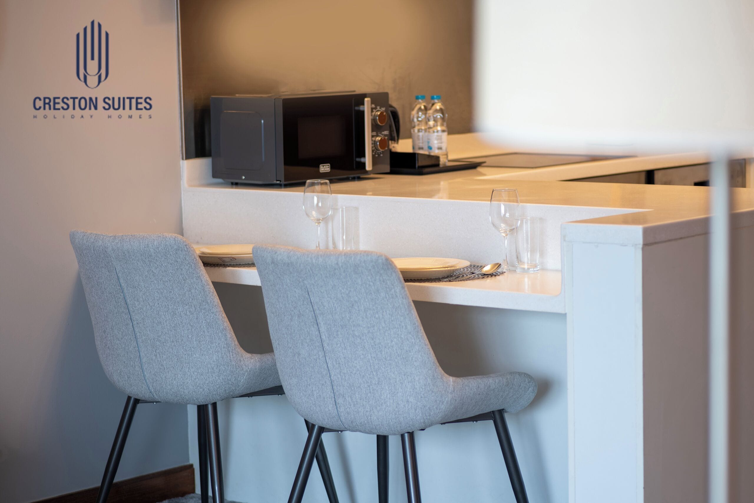 A modern kitchen area with a microwave, water bottles, and two grey chairs.