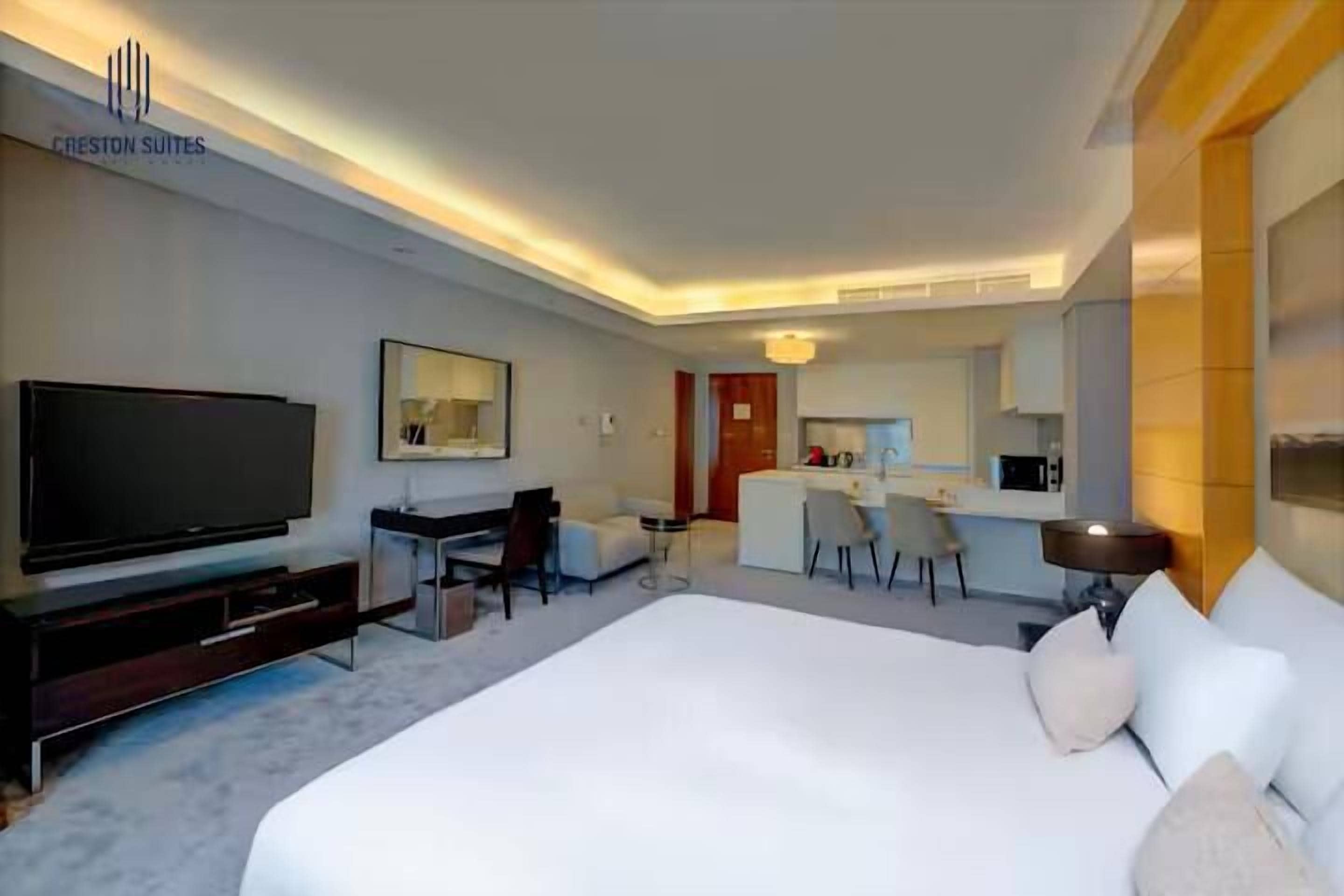 Ein modernes Hotelzimmer mit einem großen Bett, einem Fernseher, einem Schreibtisch und einer Küchenzeile.