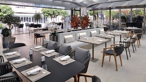 Un área de comedor al aire libre moderna con varias mesas y sillas, un sofá y plantas en macetas.