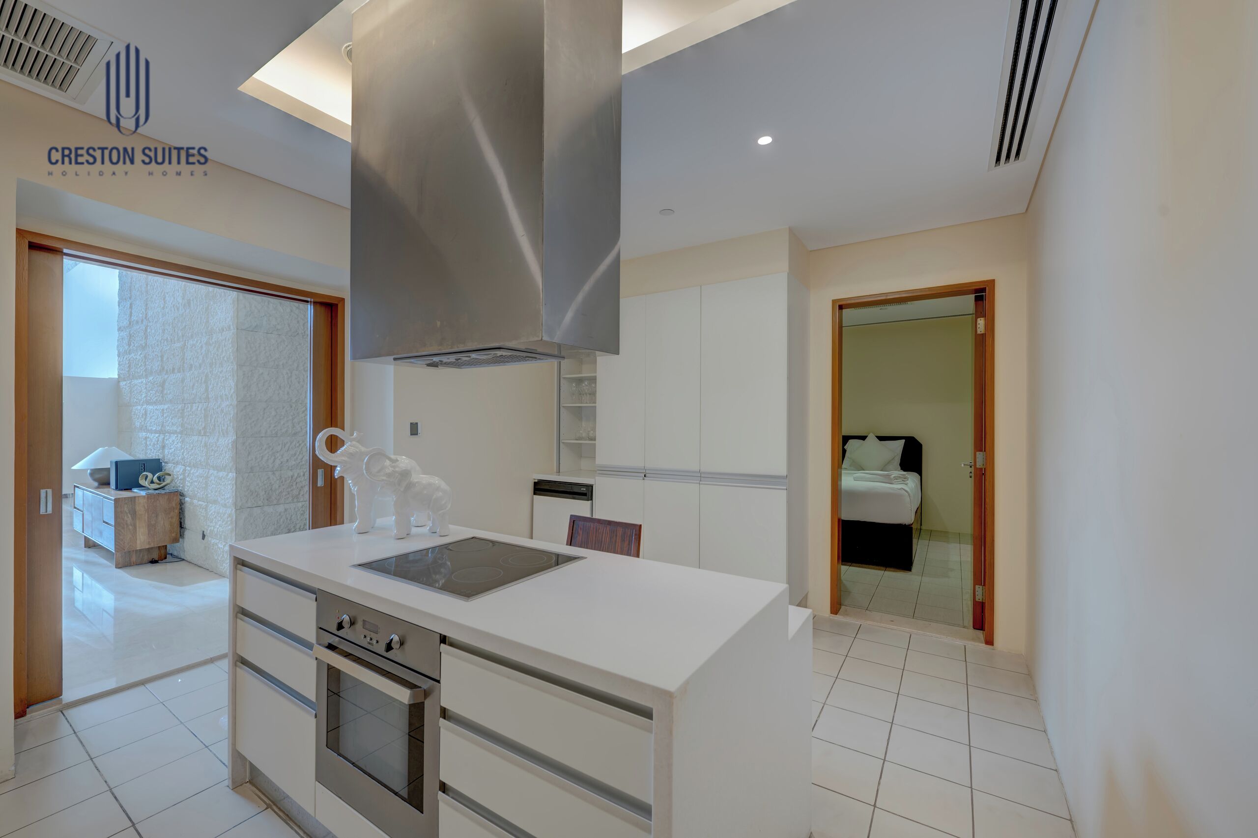 A modern kitchen with a central island, stainless steel range hood, and white cabinetry.