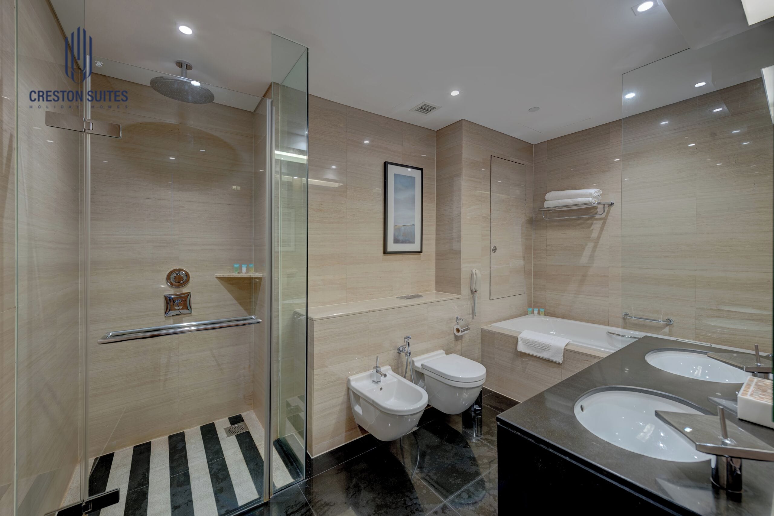 A modern bathroom with a glass shower enclosure, two bidets, a large vanity with two sinks, and a towel rack.