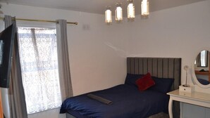 A bedroom with a bed, a bedside table, a mirror, and a window with curtains. - Modern Home Close to City Centre (Leeds)