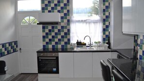 A compact kitchen with a built-in oven, a sink, and a window with curtains. - Modern Home Close to City Centre (Leeds)