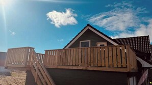 A wooden deck attached to a building with a triangular roof and a small window.