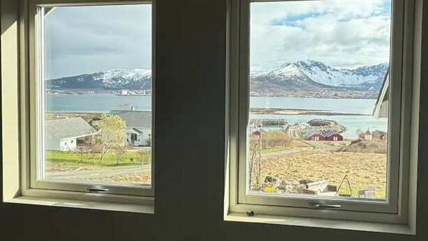 Two windows with views of a lake, mountains, and a small village. - 1 Bed Loft Sleeps 4 -hot Tub, Sauna & Pets Ok (Hadsel)