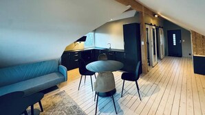 Un espacio habitable estilo loft con zona de cocina, una mesa de comedor con sillas, un sofá y una escalera que lleva a un nivel superior.
