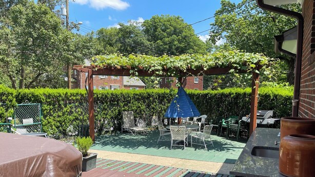 Un espace patio agrémenté d’une pergola couverte de plantes grimpantes, de mobilier d’extérieur et d’un barbecue.