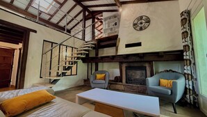 Een loft-achtige kamer met een open haard, een trap en een klok aan de muur.