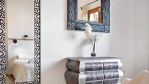 Un dormitorio con una cama, una mesita de noche con un florero y dos espejos de pared con marcos decorativos.