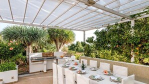 Patio esterno con zona pranzo coperta, barbecue e vegetazione rigogliosa.